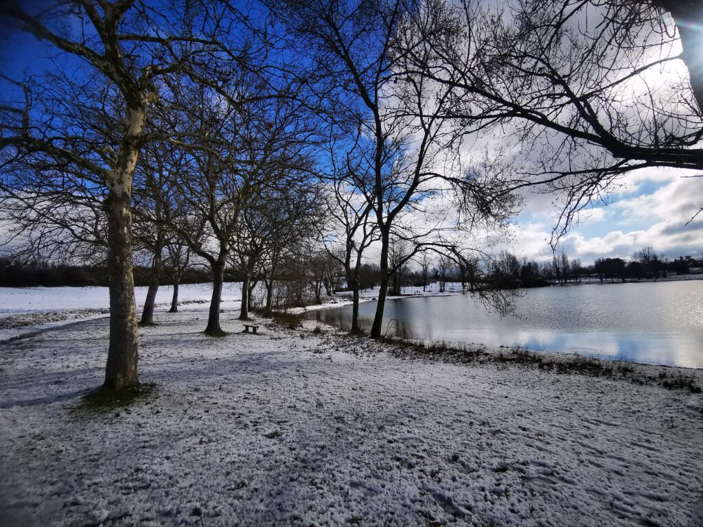 Le lac enneigé, entouré d'arbres. On distingue un coin de ciel bleu entre les nuages.